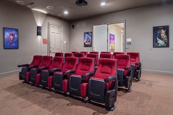 A row of red and black cinema seats are empty and facing a screen.